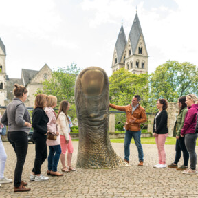 Reisegruppe hört einem Stadtführer zu, während er eine große Daumenstatue vor dem Ludwigmuseum erklärt ©Koblenz-Touristik GmbH, Dominik Ketz