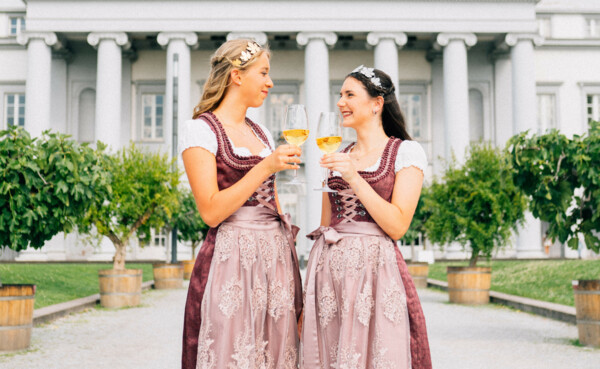 Zwei junge Frauen in festlichen Kleidern, mit Diadem und Weingläsern in der Hand, im Hintergrund das kurfürstliche Schloss in Koblenz © Koblenz-Touristik GmbH, Tibor Resch